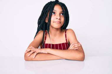 Saçları örgülü genç Afro-Amerikalı kız masaya oturmuş gülümsüyor ve yan tarafa bakıyor ve şöyle düşünüyor:. 