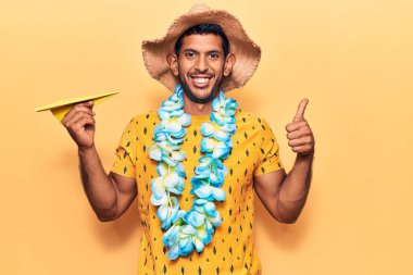 Yaz şapkası takan genç latin adam ve elinde kağıt uçak tutan Hawaii zambağı mutlu ve olumlu gülümsüyor, başparmağıyla mükemmel ve onay işareti yapıyor. 
