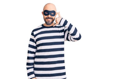 Hırsız maskesi takan, gülümseyen, el ve parmaklarıyla telefonla konuşan genç yakışıklı bir adam. iletişim kavramları. 