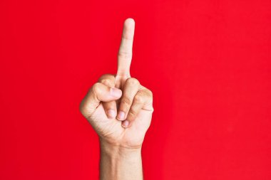 Arm of caucasian white young man over red isolated background showing provocative and rude gesture doing fuck you symbol with middle finger 