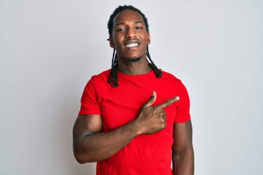 Saçları örgülü, neşeli kıyafetler giyen, yüzünde mutlu ve doğal bir ifadeyle elleri ve parmaklarıyla yüzünü gösteren bir gülümseme olan Afrikalı Amerikalı bir adam. 