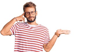 Sıradan kıyafetler ve gözlük takan sakallı yakışıklı sarışın adam. Avuç içinin içi açık, fotokopi alanı ve alnını göstermekten rahatsız oluyor. Bunu bir düşün.. 