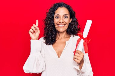 Orta yaşlı, diploma almış güzel bir kadın bir fikir veya soruyla gülümsüyor ve mutlu bir yüzle işaret ediyor. 