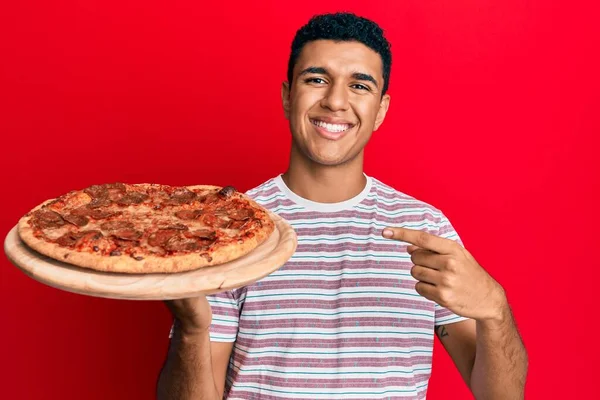 Jonge Arabisch Man Houdt Italiaanse Pizza Glimlachend Gelukkig Wijzend Met — Stockfoto