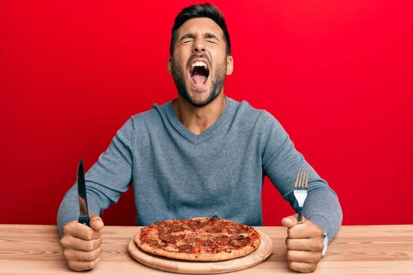 Hombre Hispano Guapo Comiendo Sabrosa Pizza Pepperoni Enojado Loco Gritando —  Fotos de Stock