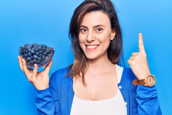 Elinde böğürtlen tutan genç ve güzel bir kadın bir fikirle ya da soru sorarak gülümsüyor ve mutlu bir yüzle işaret ediyor. 