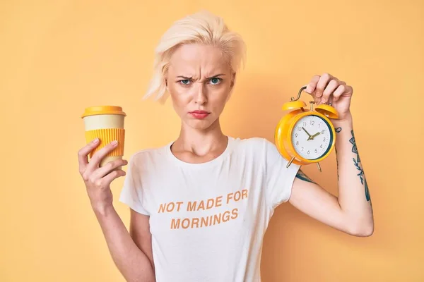 タトゥーの目覚まし時計を保持し コーヒー懐疑的で緊張のカップを奪う若いブロンドの女性は 問題のために動揺を眉をひそめて 否定的な人 — ストック写真