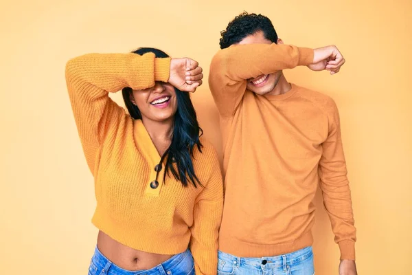 Güzel, genç, latin bir çift, günlük giysiler giyip, gözleri kollarıyla kapatarak neşeli ve komik gülümsüyor. kör kavram. 