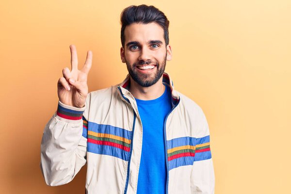 Young handsome man with beard wearing casual jacket showing and pointing up with fingers number two while smiling confident and happy. 