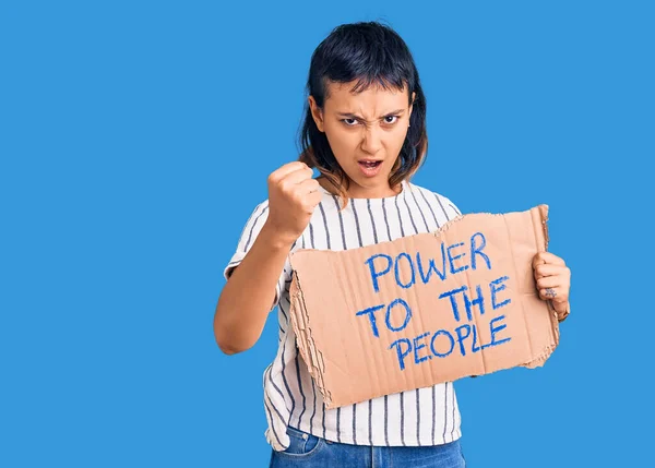 Young woman holding power to the people banner annoyed and frustrated shouting with anger, yelling crazy with anger and hand raised