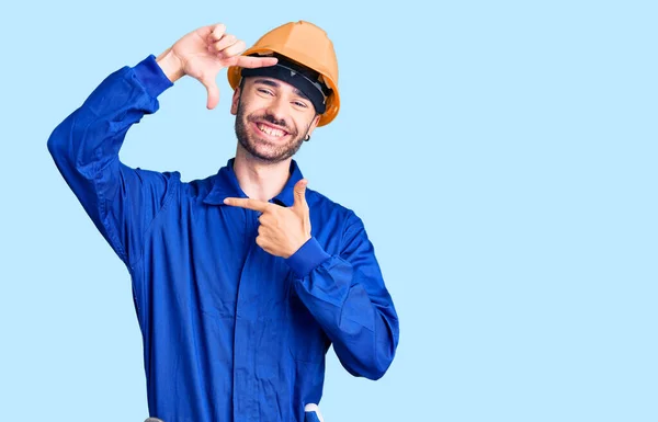 労働者の制服を着た若いヒスパニック系の男が幸せな顔をした手と指で笑顔のフレームを作ります 創造性と写真の概念 — ストック写真