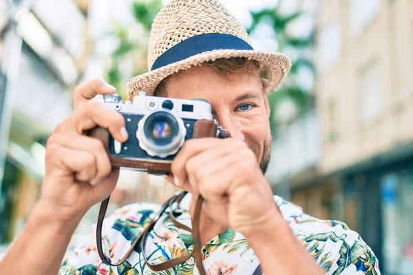 夏の帽子と花のシャツを身に着けているハンサムな白人男性は ヴィンテージカメラを使用して屋外で写真を撮る幸せな笑顔 — ストック写真