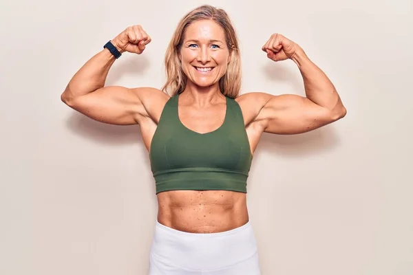 Blonde caucasian middle age sports woman posing and showing arms strength over isolated background