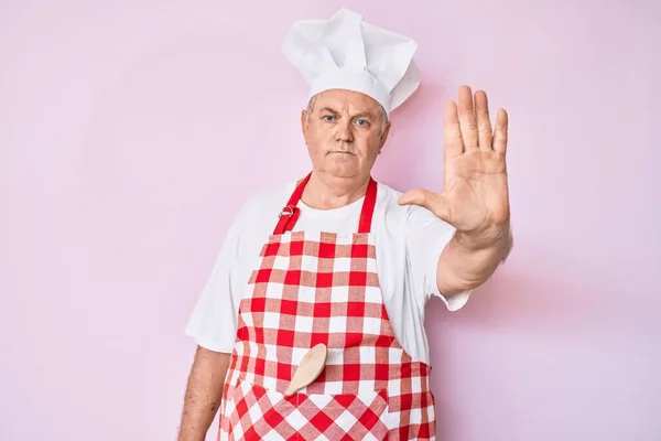 年长的白发男子穿着专业的烘焙者围裙 手心停止歌唱 用消极而严肃的手势警告人 — 图库照片