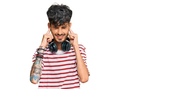 年轻的惊慌失措的男人用耳机用手指捂住耳朵 用恼怒的表情听着嘈杂的音乐 聋人概念 — 图库照片