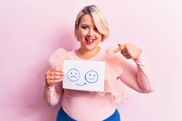 Young blonde plus size woman asking for positive change holding paper with emotion message smiling happy pointing with hand and finger