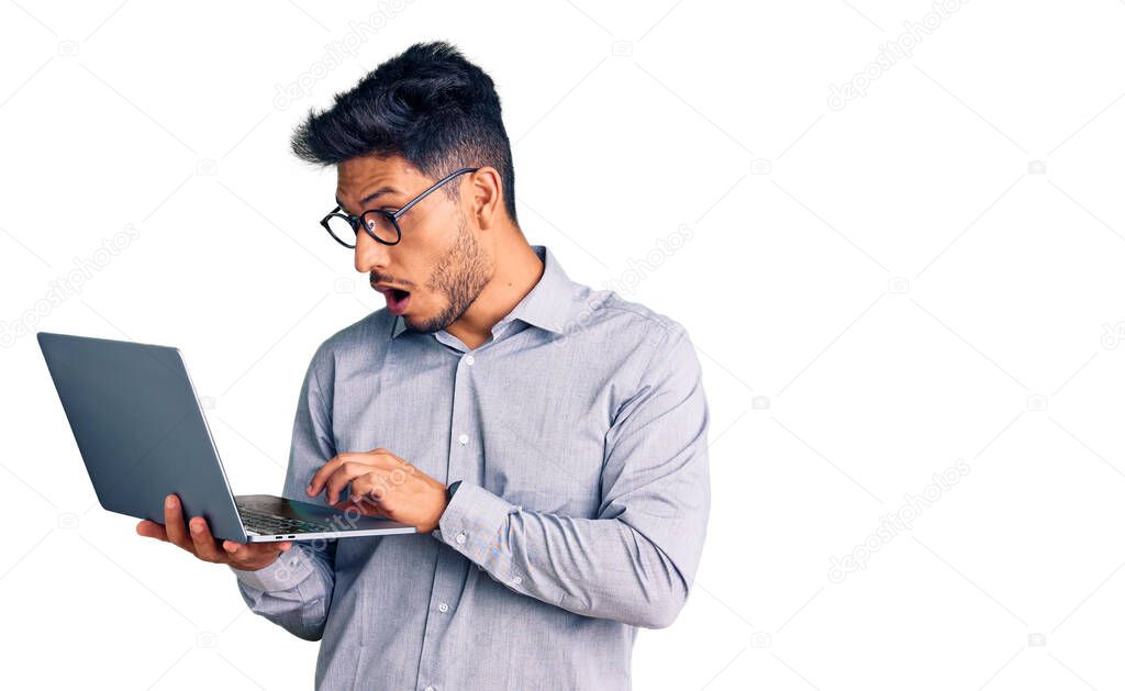 Handsome latin american young man working using computer laptop scared and amazed with open mouth for surprise, disbelief face 