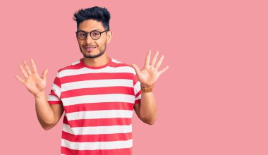 Yakışıklı Latin Amerikalı gündelik kıyafetler ve gözlük takan genç adam on numarayı gösterip işaret ederken kendinden emin ve mutlu gülümsüyor.. 