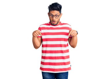 Yakışıklı Latin Amerikalı gündelik kıyafetler giyen ve gözlüklü genç adam parmaklarını göstererek reklamını yapıyor, şaşırmış bir yüz ve açık bir ağız. 
