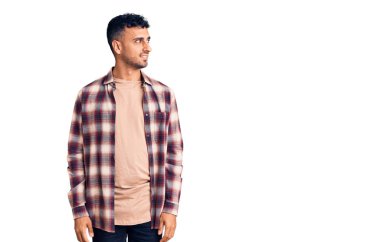 Gündelik kıyafetler giyen genç İspanyol bir adam yüzünde gülümsemeyle yan yana bakıyor, doğal bir ifade. Kendinden emin gülen. 