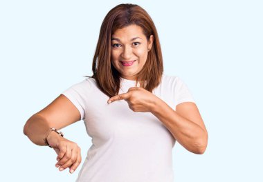 Orta yaşlı, beyaz tişört giyen Latin bir kadın acele ederek saati, sabırsızlığı ve gecikmeyi izlemek istiyor. 