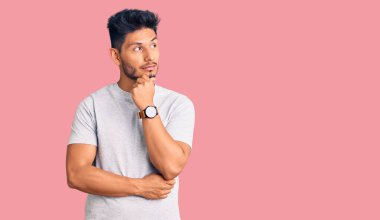 Yakışıklı Latin Amerikalı genç adam. Elleri çenesinde gündelik tişört giyiyor. Soru sormayı, düşünceli ifadeyi düşünüyor. Düşünceli bir yüzle gülümsüyor. şüphe kavramı. 