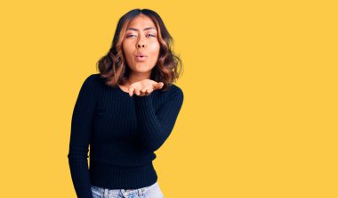 Genç, güzel, melez bir kadın, gündelik kıyafetler giyip kameraya bakıyor ve havada el sallayarak öpüşüyor. Güzel ve seksi. aşk ifadesi. 