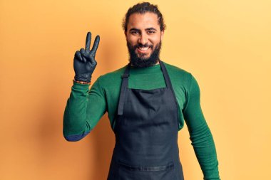 Berber önlüğü giymiş genç bir Arap kameraya gülümseyen ve zafer işareti yapan bir adam. İki numara.. 