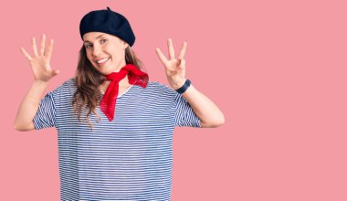 Fransız beresi ve çizgili tişört giyen genç ve güzel sarışın kadın sekiz numaralı parmaklarını gösterip gösterirken kendinden emin ve mutlu bir şekilde gülümsüyor.. 