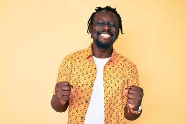Saçları örgülü, başarılı olmak için heyecanlı kolları havada, gözleri kapalı zaferi kutlayan genç Afro-Amerikan bir adam. Kazanan konsept. 