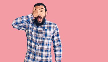 Gündelik kıyafetler giyen genç Arap adam şok içinde yüzünü ve gözlerini kapayarak utanmış ifadesiyle parmaklarının arasından bakıyor.. 