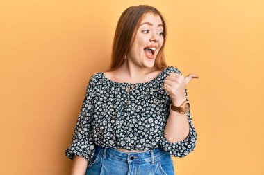 Çiçek desenli tişört giyen güzel, kızıl saçlı bir kadın baş parmağını kaldırıyor ve ağzı açık gülümsüyor. 