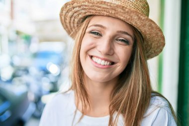 Genç sarışın kadın tatilde gülümsüyor. Mutlu bir şekilde şehrin duvarına yaslanıyor.