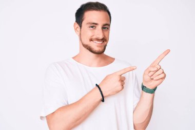 Gündelik beyaz tişört giyen genç yakışıklı adam gülümseyip kameraya bakıyor ve iki eliyle ve parmaklarıyla kenarı gösteriyor.. 