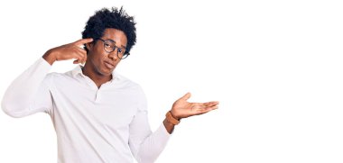 Afro saçlı, sıradan giyinmiş, gözlüklü, kafası karışmış ve avuç içi açık, fotokopi alanı gösteren ve alnını işaret eden yakışıklı Afro Amerikalı bir adam. Bunu bir düşün.. 