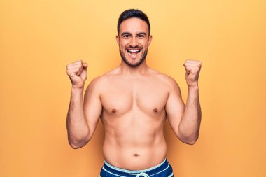 Sakallı, kolsuz tişörtlü genç yakışıklı sarı arka planda durup gururla bağırıyor zaferi ve başarıyı kollarını kaldırarak kutluyor.