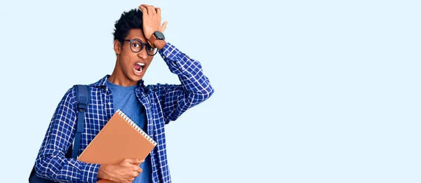 Joven Afroamericano Hombre Usando Mochila Estudiante Celebración Libro Sorprendido Con —  Fotos de Stock