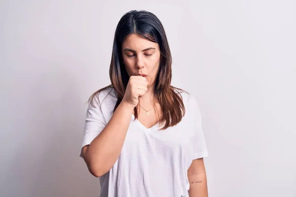 若い美しいブルネットの女性は寒さや気管支炎の症状としてよくないと咳をする孤立した白い背景感の上に立ってカジュアルなTシャツを着ています ヘルスケアの概念 — ストック写真
