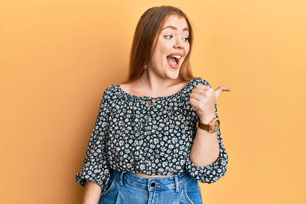 Çiçek desenli tişört giyen güzel, kızıl saçlı bir kadın baş parmağını kaldırıyor ve ağzı açık gülümsüyor. 