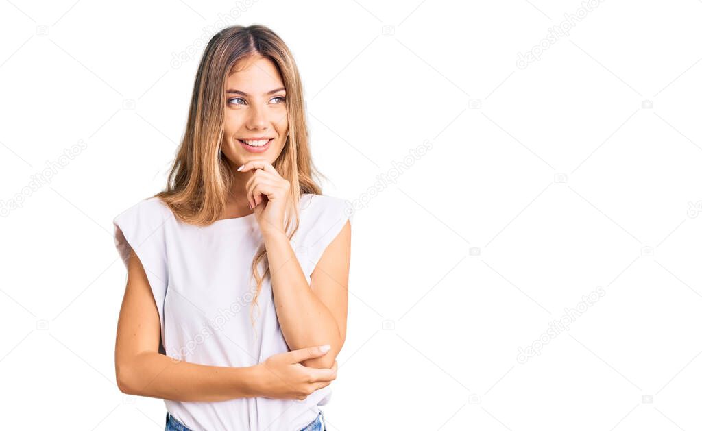 Beautiful caucasian woman with blonde hair wearing casual white tshirt with hand on chin thinking about question, pensive expression. smiling with thoughtful face. doubt concept. 