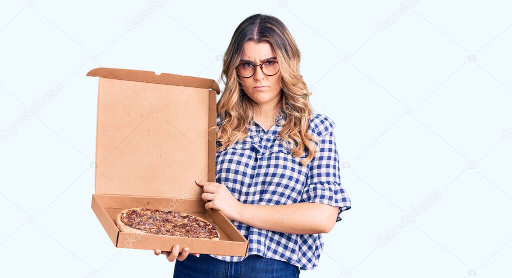 Young caucasian woman holding delivery pizza box thinking attitude and sober expression looking self confident 