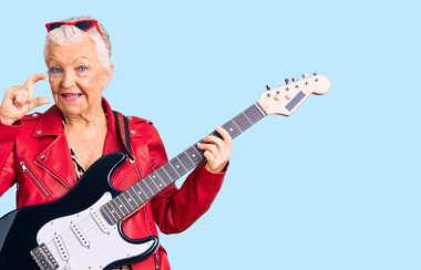 Son sınıf güzeli, mavi gözlü, gri saçlı, modern görünümlü, gitar çalan, gülümseyen, kendine güvenen, el hareketi yapan, parmaklarıyla işaret yapan ve kameraya bakan bir kadın. ölçüm kavramı. 
