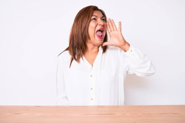 Orta yaşlı esmer, Latin iş kadını, gündelik beyaz gömlekli, masada oturmuş el ele tutuşarak bağırıyor ve çığlık atıyordu. iletişim konsepti. 