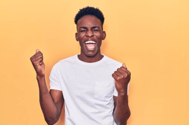 Gündelik giysiler giyen genç Afro-Amerikalı adam kolları havada ve gözleri kapalı bir şekilde başarıyı kutluyor ve şaşırıyor. Kazanan konsept. 