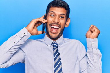 Genç latin adam telefonda konuşuyor gururla bağırıyor, zaferi kutluyor ve kollarını kaldırarak heyecanlanıyor. 