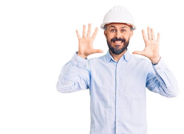 Mimar kasketi takan genç yakışıklı adam on numarayı gösterip işaret ederken kendinden emin ve mutlu bir şekilde gülümsüyor.. 