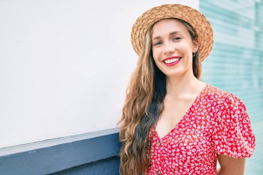 Genç sarışın kadın tatilde gülümsüyor. Mutlu bir şekilde şehrin duvarına yaslanıyor.