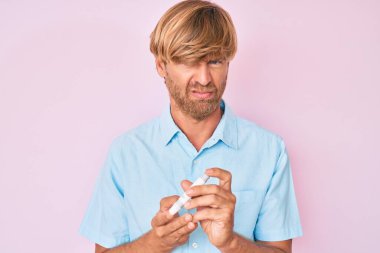 Genç sarışın adam glikoz ölçer kullanıyor şüpheci ve gergin, sorun yüzünden surat asıyor. negatif kişi. 