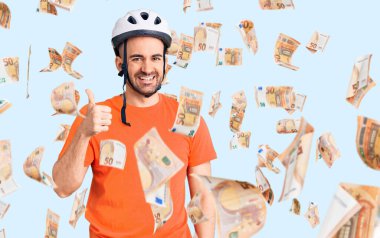 Bisiklet kaskı takan genç, mutlu ve pozitif gülümseyen, başparmağıyla mükemmel ve onay işareti yapan yakışıklı bir adam.