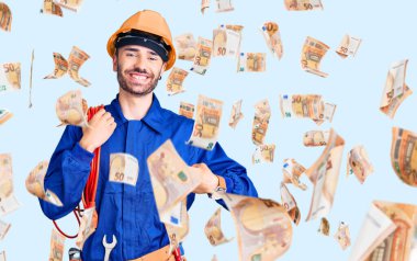 Genç İspanyol adam, elektrokrat üniforması içinde elinde kabloyla mutlu ve gururlu bir şekilde gülümseyen birini işaret ediyor.